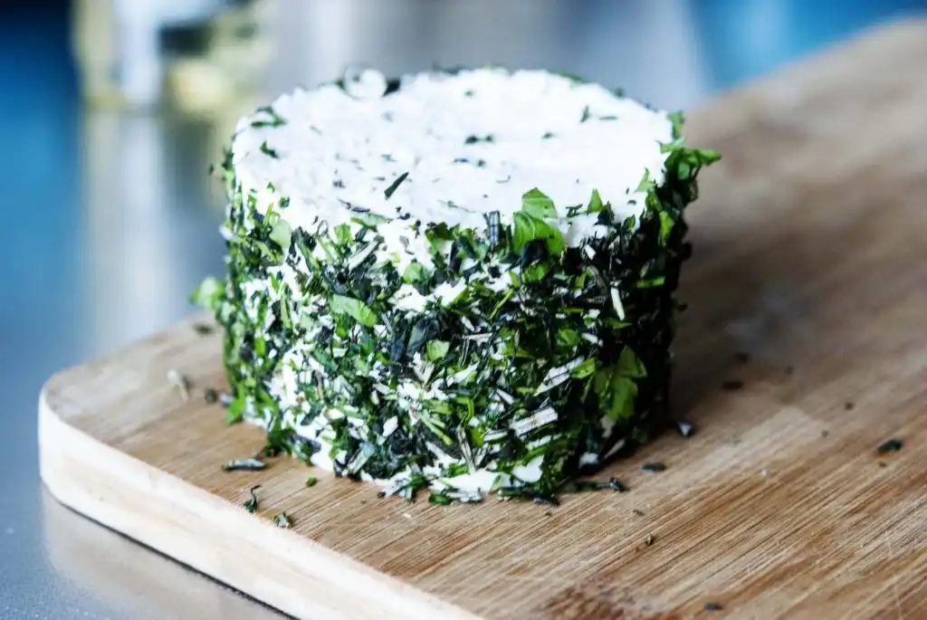 Бял сирен блок на дървена дъска покрит със зелени подправки.