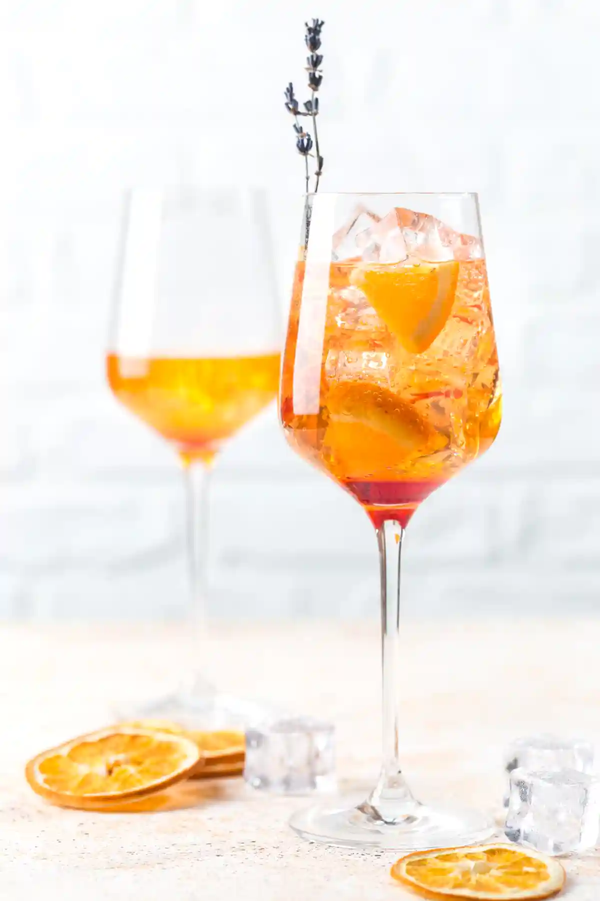 Две чаши Аперол Шприц с лед и резени портокал, сервирани със сушени портокалови кръгчета.