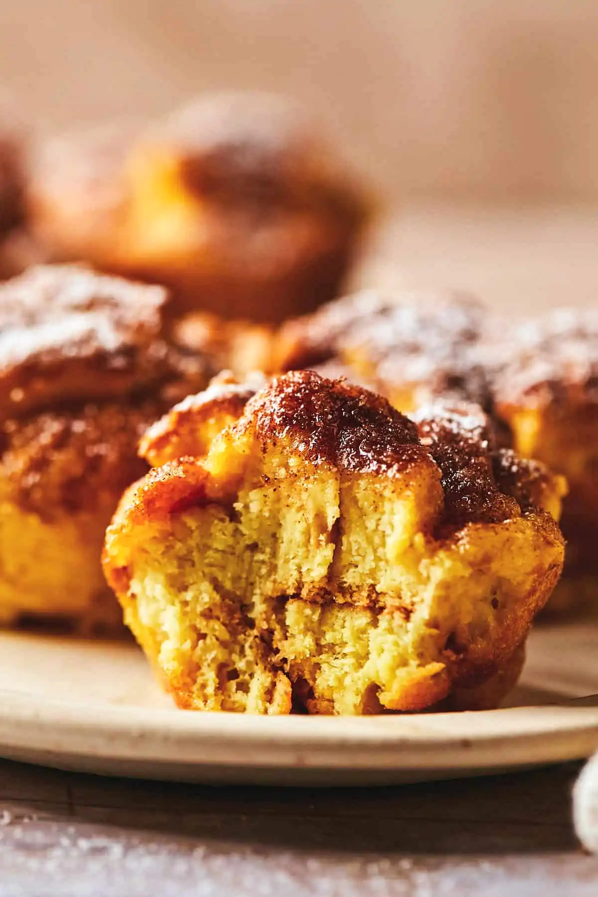Сочни мъфини с вкус на френски тост, поръсени с канела и пудра захар, сервирани върху чиния.