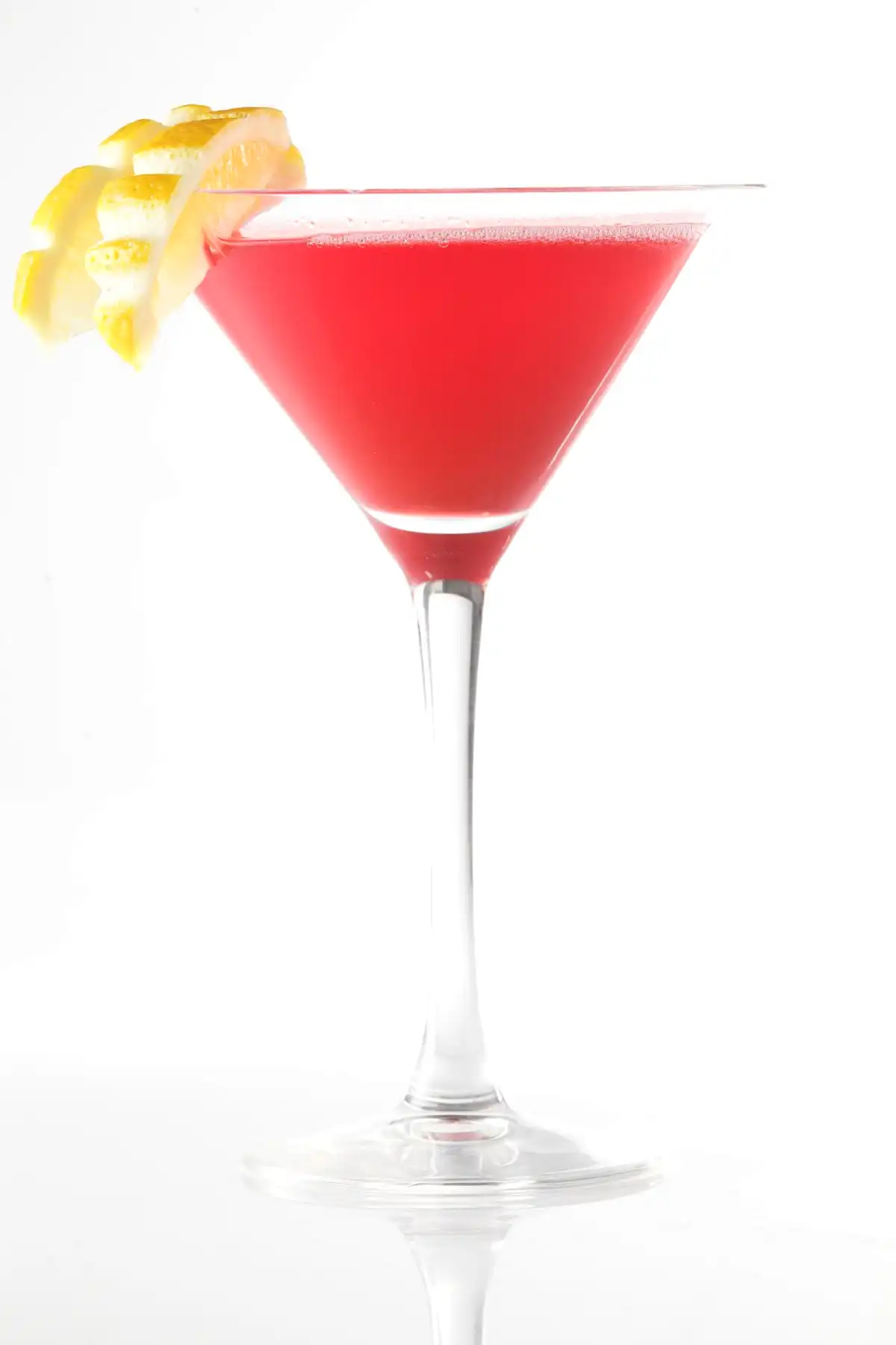 Червен коктейл във висока чаша за мартини, украсена с навита лимонова кора на ръба, поставена на бял фон.