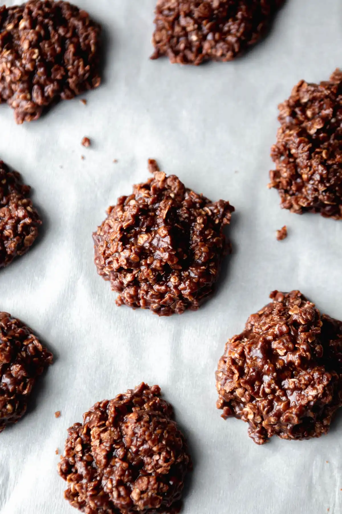 Бисквитки от шоколадови зърнени храни, разположени върху хартия за печене. Бисквитките са с неправилна форма и гланцова текстура, характерни за сместа от течен шоколад и зърнени храни.