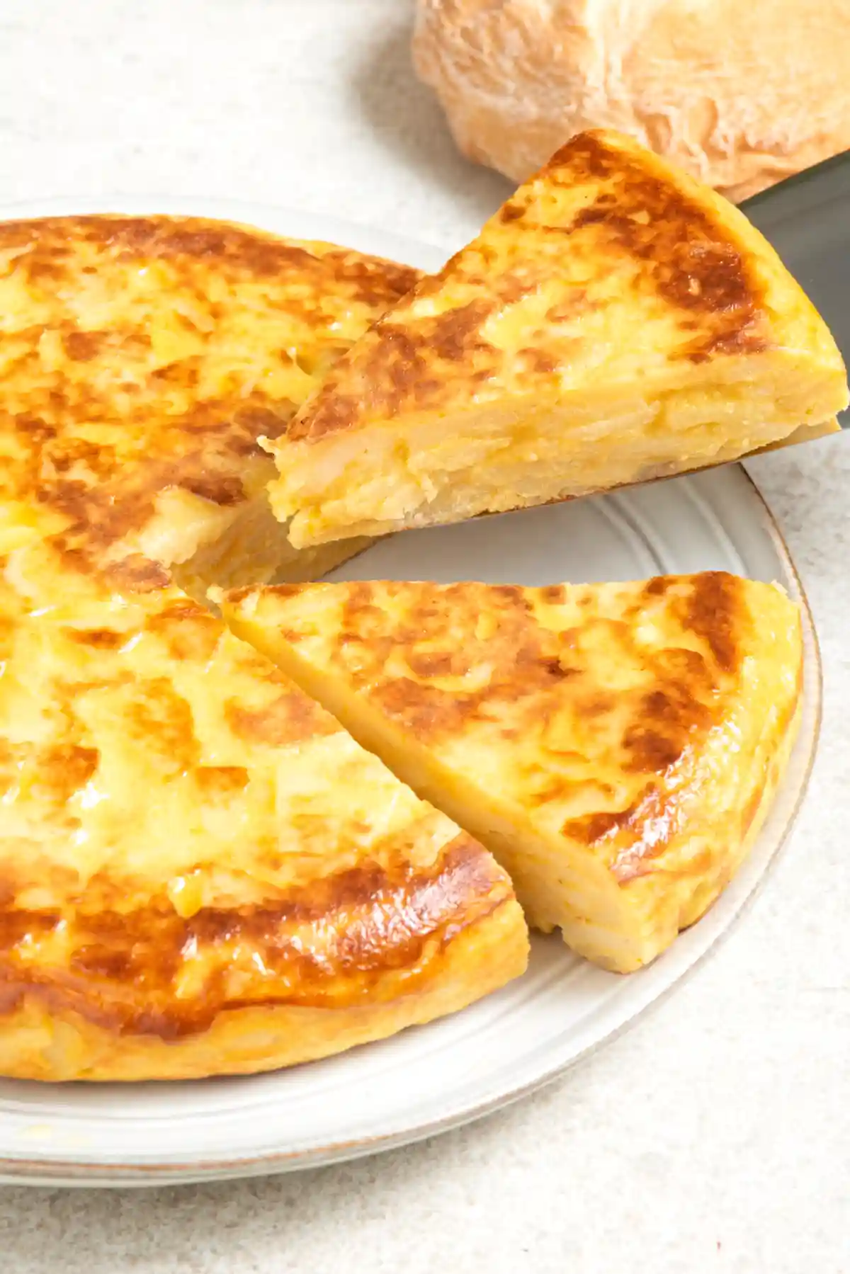 Торта от картофи, нарязана на триъгълни парчета, на чиния със заострен ръб. Две парчета са леко издигнати, готови за сервиране, показващи златисто-кафявата, хрупкава повърхност и меката вътрешност. На фона се вижда част от друго парче тесто.