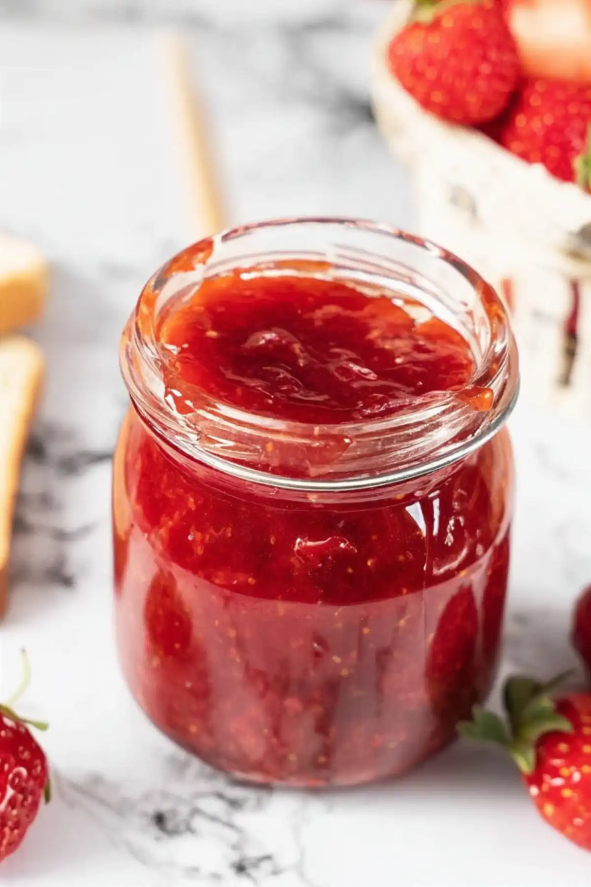 Отворен стъклен буркан с ярко червено ягодово сладко, намазано богато по вътрешната страна на буркана, на фона на мека светлина и неясно виждащи се обекти.